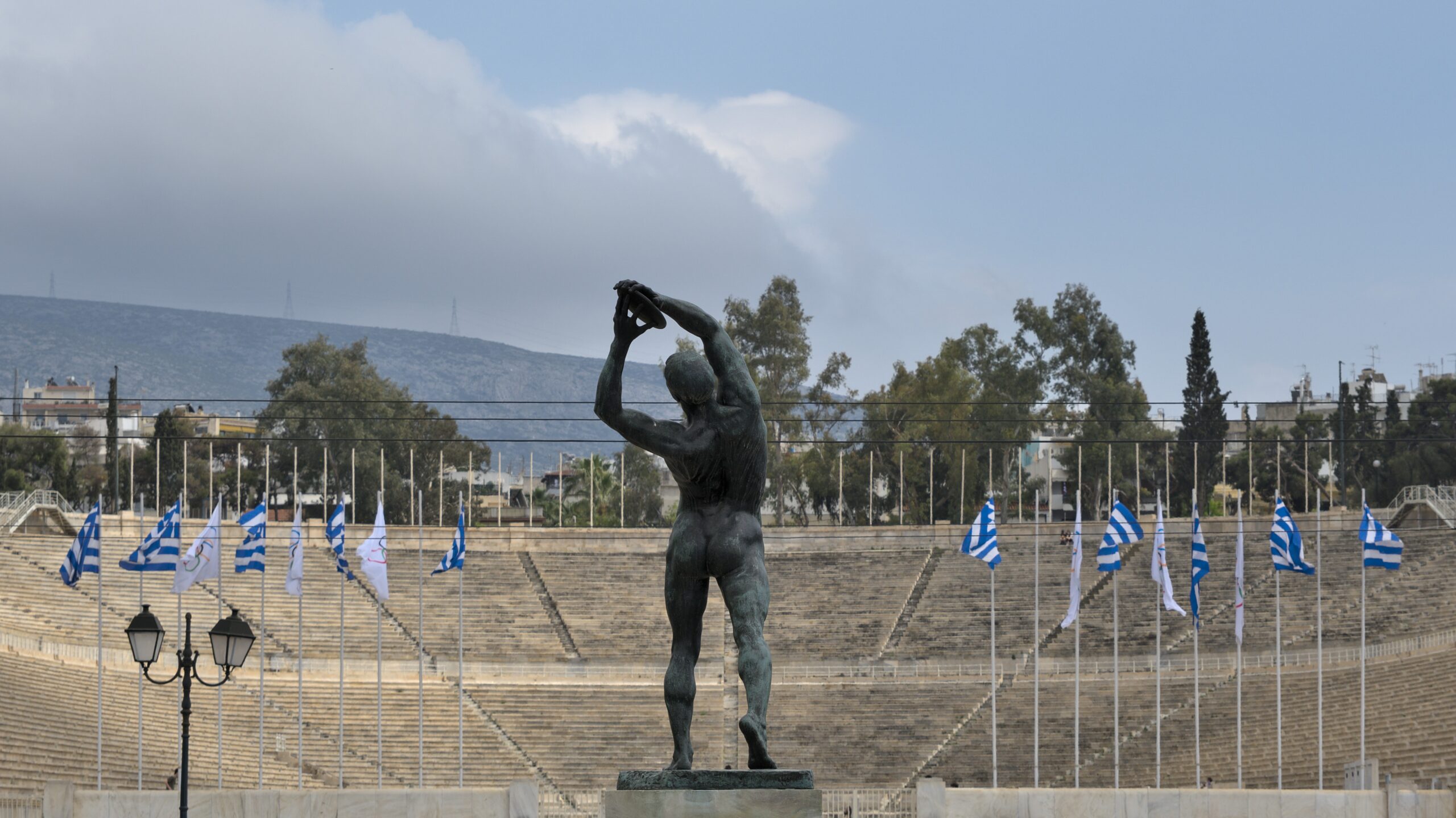 Patung atlet dan stadion Panathenaic di Athena, Yunani, dengan deretan bendera Yunani dan Olimpiade.